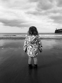 Rear view of child walking on beach against sky