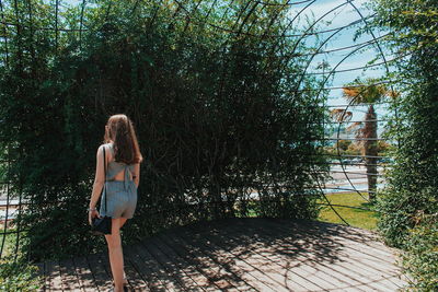 Rear view of young woman standing against trees