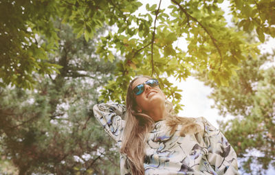 Low angle view of woman wearing sunglasses against trees