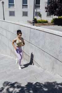 Young female athlete running on steps by surrounding wall