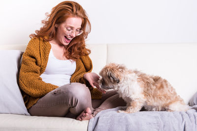 Woman playing with dog while sitting on sofa at home