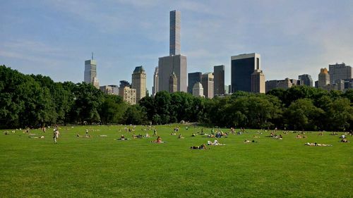 Panoramic view of people on field by buildings against sky