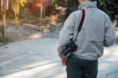 Rear view midsection of man with digital camera standing on street