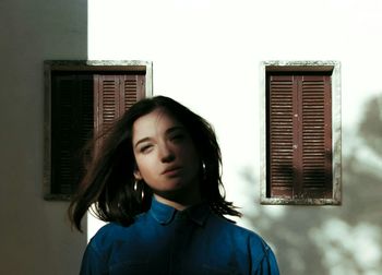 Portrait of young woman standing against building