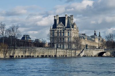 Palais du louvre by the seine against cloudy sky