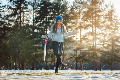 Full length of mid adult woman playing with snow on field against trees in forest