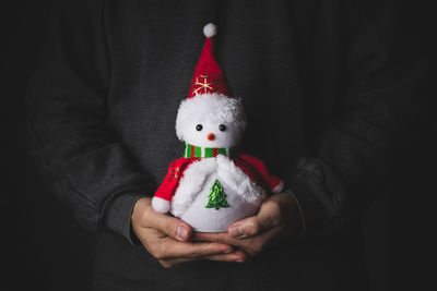 Midsection of person holding snowman against black background