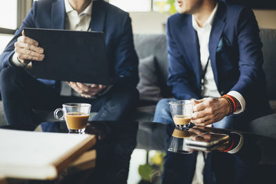 Midsection of businessman showing laptop to colleague while sitting on sofa at workplace