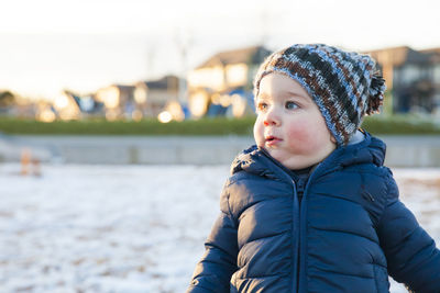 Cute boy looking away while standing at playground during winter