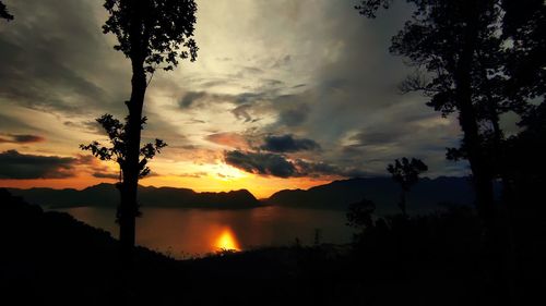 Silhouette trees by lake against sky during sunset