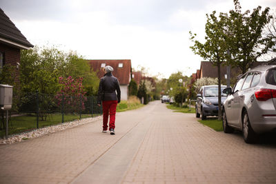 Rear view full length of man walking on footpath by houses