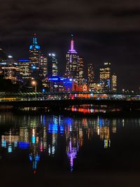 Illuminated buildings by river against sky at night