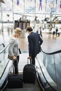 Rear view of business people with luggage moving down escalator at airport