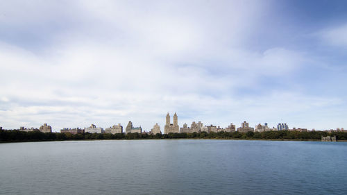 City at waterfront against cloudy sky