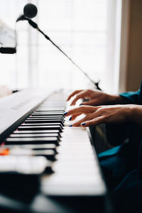 Cropped image of woman playing piano by window at studio