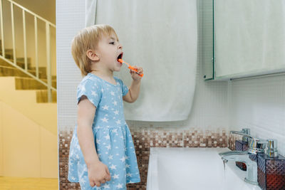 A little girl learns to brush her teeth on her own in the bathroom.