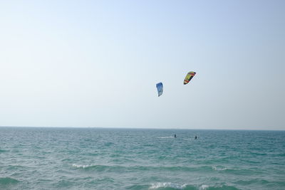 Person paragliding over sea against clear sky