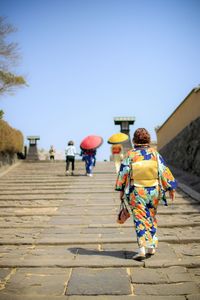 Rear view of woman wearing kimono walking on footpath against clear sky