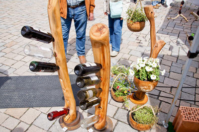 Low section of people standing on footpath by potted plants and beer bottles on wood