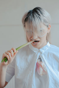 Close-up portrait of woman with painted face eating scallion against white background