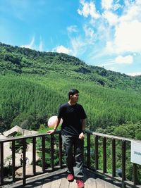 Full length of young man looking away while standing by railing against sky