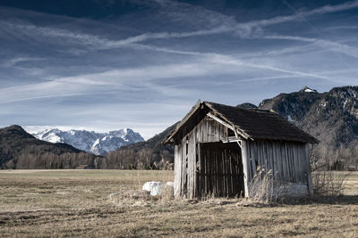 Wooden house on field by mountains against sky