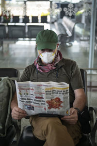 Middle aged man reads about covid-19 while waiting at a deserted airport in khajuraho, madhya pradesh, india, wearing a face mask to stay protected.