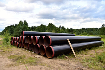 Stack of pipes on field against sky