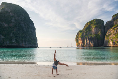 Rear view of woman standing at beach against sky