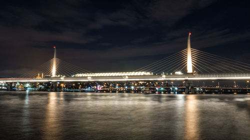 Illuminated bridge over river against sky at night