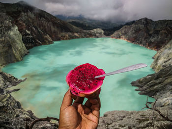 Cropped hand of person holding pitaya by lake