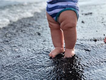 Low section of baby standing at beach