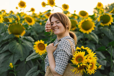 Beautiful young woman with sunflowers enjoying nature and laughing on summer sunflower field.