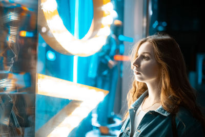 Portrait of young woman looking at illuminated mirror