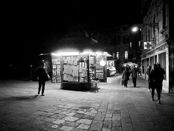 Rear view of people walking on illuminated street at night
