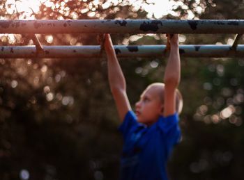 Side view of boy hanging on monkey bars at playground during sunset