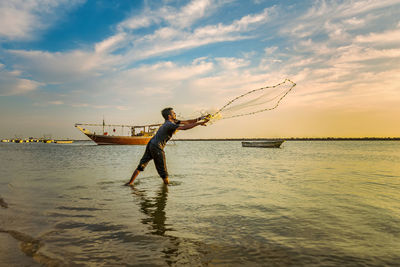 Man standing in sea against sky during sunset