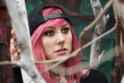 Young woman with pierced face and tattooed neck behind tree branches