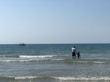 Rear view of men on beach against clear sky