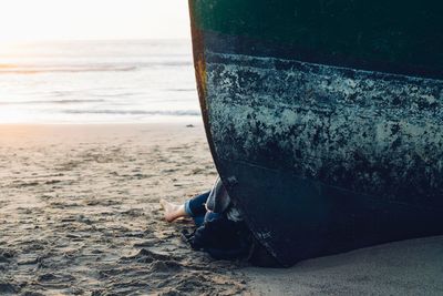 Low section of person sitting by boat moored at beach