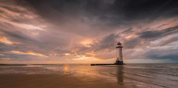 Lighthouse by sea against sky during sunset