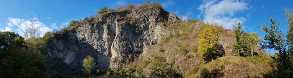 Low angle view of panoramic shot of rock formation amidst trees against sky