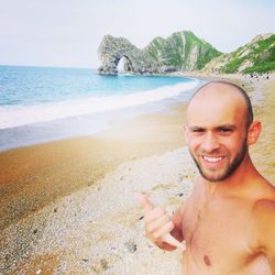 Portrait of shirtless man standing at beach against sky