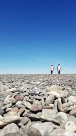 People on rocks against clear blue sky