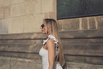 Side view of woman wearing sunglasses standing against wall