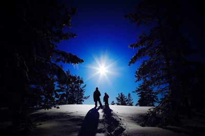 Rear view of silhouette people walking on snow covered field sunny day