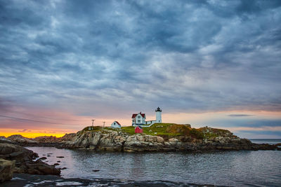 Lighthouse by sea against sky during sunset