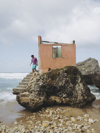 Man on steps of abandoned built structure at beach against sky