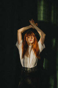 Portrait of young woman standing against black background