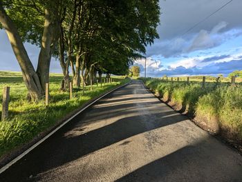 Empty road amidst trees against sky
